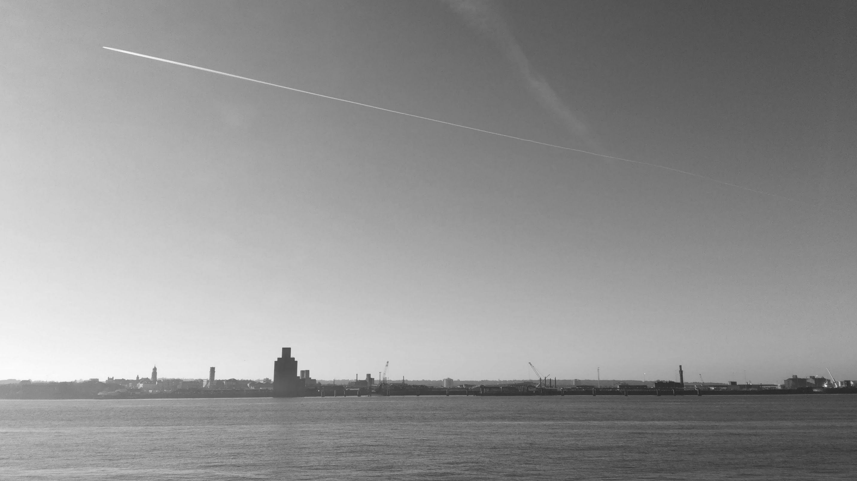 Most of the image is a plain monochrome sky, with a lonely aeroplane passing through it. At the bottom runs the River Mersey.