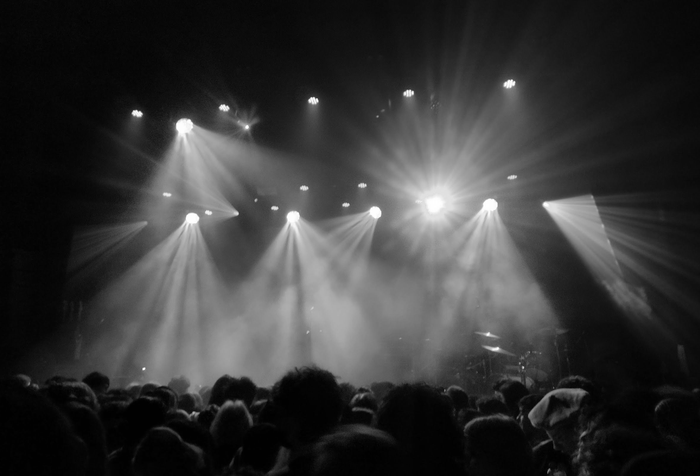 You are at the back of a crowd in a concert hall. The lights are shining, the drum kit is gleaming, but there is no one to play