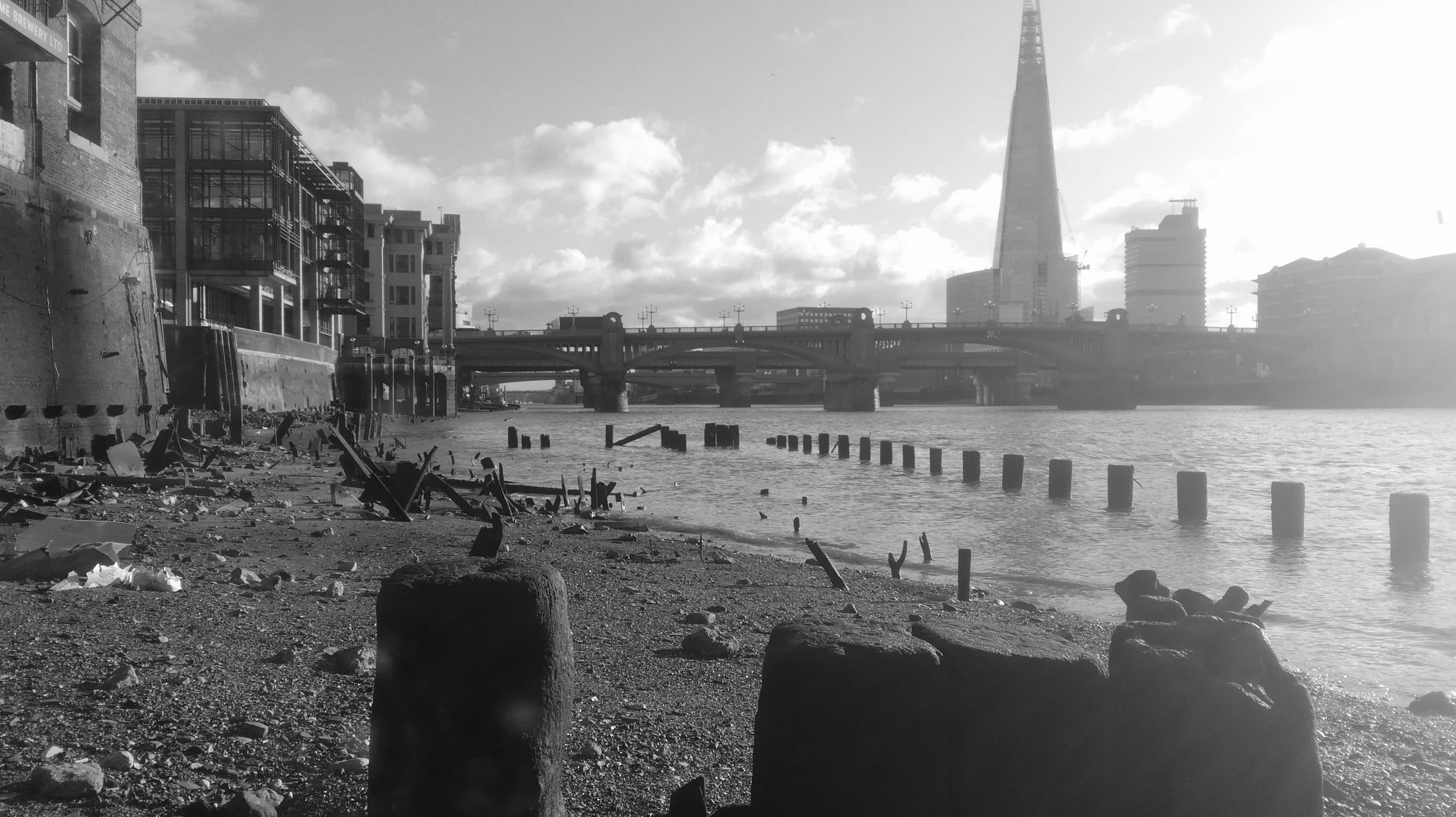 A view of the River Thames. Long ago, a building used to stand where you are, but now all that is left is the foundations. Across the river, there is a modern building, a sharp triangle. 
